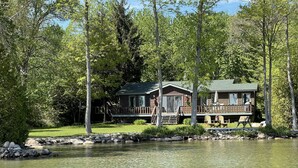 A cabin with a deck overlooking a lake, surrounded by trees. - Waterfront & Pvt Beach 120’Shoreline: SHALLOW/Sandy: Perfect for Little Kids! (Brechin)