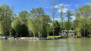 A lakeside cabin with a deck and outdoor seating, surrounded by trees and a clear lake. - Waterfront & Pvt Beach 120’Shoreline: SHALLOW/Sandy: Perfect for Little Kids! (Brechin)