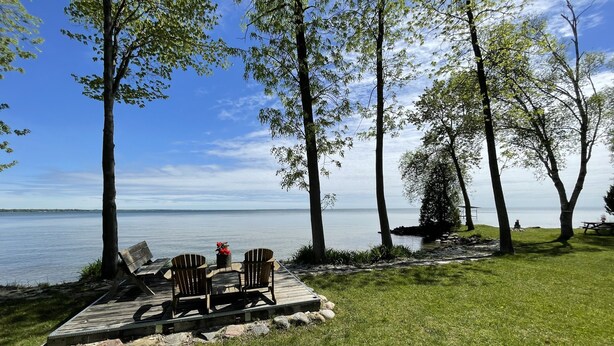 A lakeside deck with a table and chairs, surrounded by trees and overlooking a calm lake. - Waterfront & Pvt Beach 120’Shoreline: SHALLOW/Sandy: Perfect for Little Kids! (Brechin)