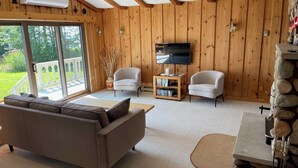 A cozy living room with a sofa, two armchairs, a TV, and a stone fireplace. - Waterfront & Pvt Beach 120’Shoreline: SHALLOW/Sandy: Perfect for Little Kids! (Brechin)