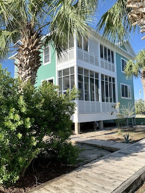Uma casa de dois andares com varanda, cercada por vegetação e um deck de madeira.