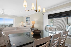 Uma sala de estar moderna com uma mesa de jantar de vidro, sofás brancos e um ventilador de teto.