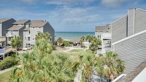 Una zona residencial costera con varios edificios de dos pisos, vista despejada al océano y un césped cuidado con palmeras.