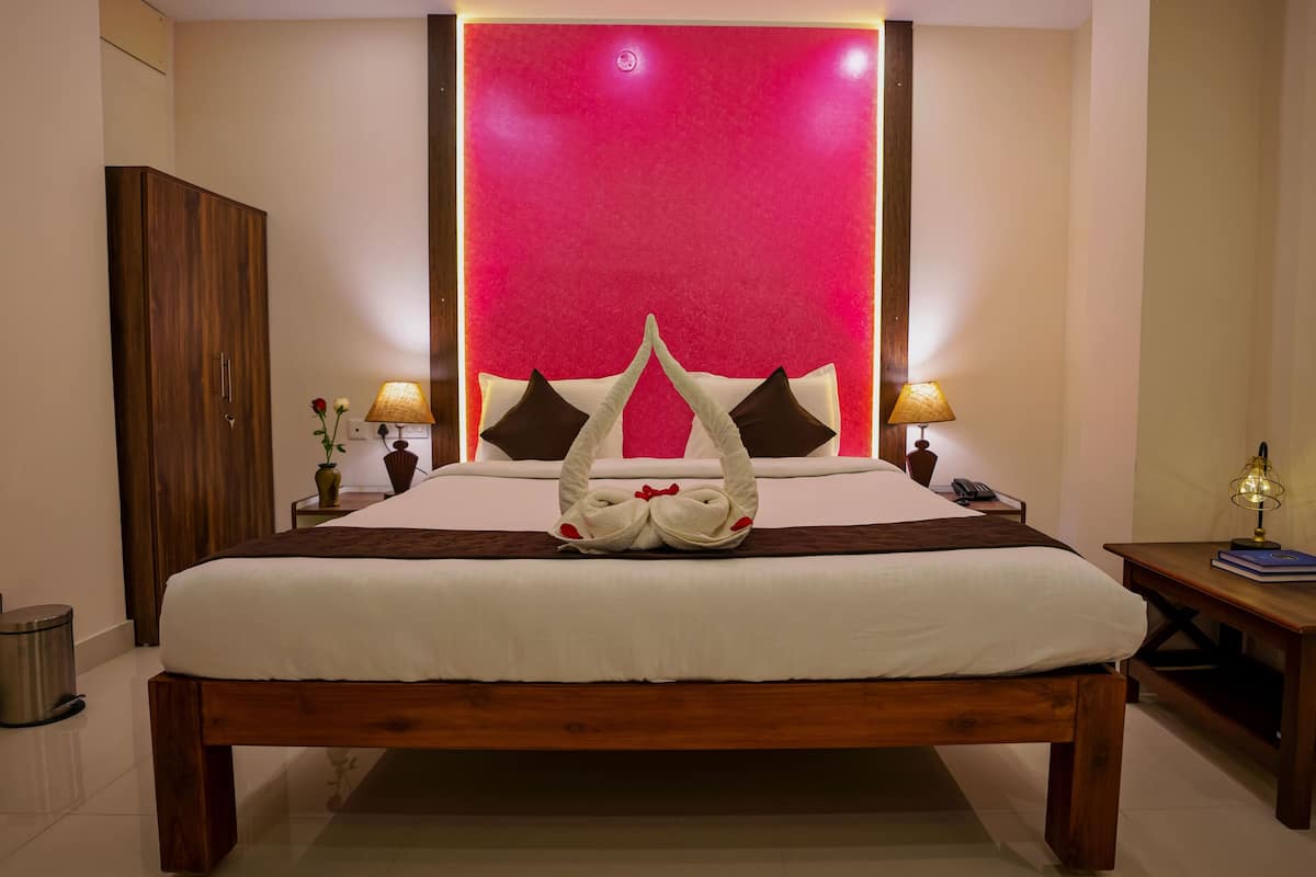 A neatly made bed with a wooden frame, two bedside tables with lamps, a trash bin, and a large wall with a red panel.