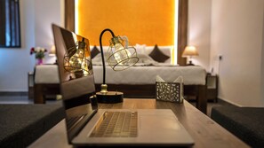 A laptop on a wooden table with two decorative lamps, a tissue box, and a bed in the background. - Sai Senthoor Paradise (Puducherry)