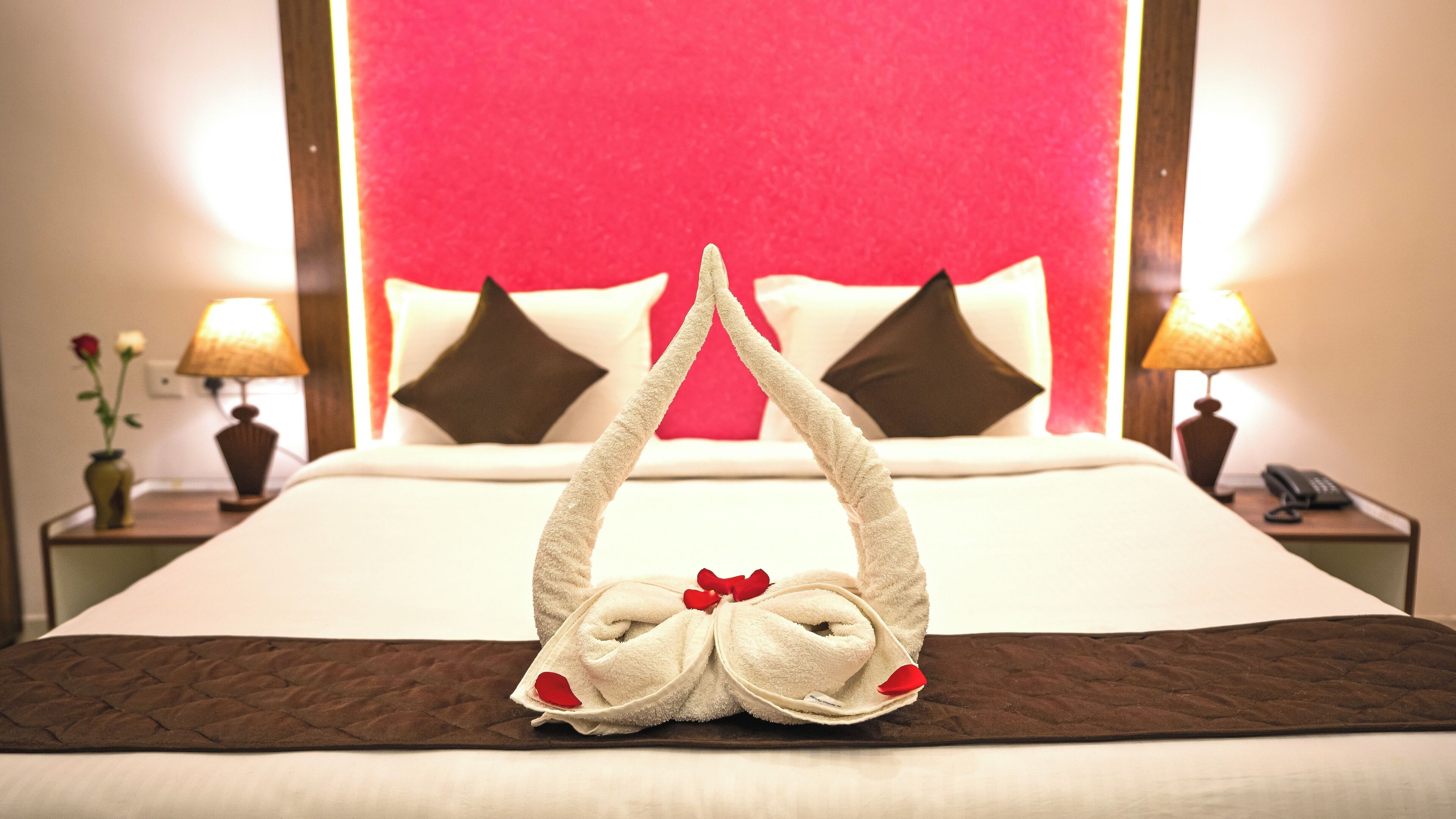A hotel room with a bed, pillows, a blanket, and a towel artfully arranged on the bed.
