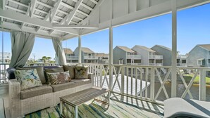 A covered balcony with a sofa, a small table, and a chair. The balcony overlooks a residential area with houses and a body of water. - Fall 2026 Rate Drop! 3 BR/3 BA Cottage -Dog Friendly! (Port St. Joe)