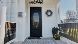 A white house with a black front door, a welcome sign, a wreath, and a US Mail sign. - Two Hearts Rambling Rose (Hermann)
