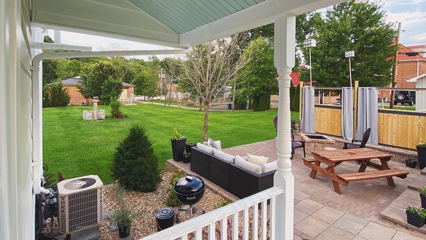 A covered patio with a white railing, a wooden table, and a grill. - Two Hearts Rambling Rose (Hermann)