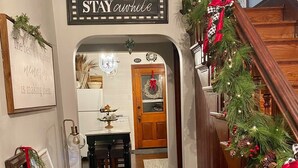 A hallway with a wooden staircase, decorated with Christmas garlands and lights. A sign above the staircase reads "STAY awhile". - Two Hearts Rambling Rose (Hermann)