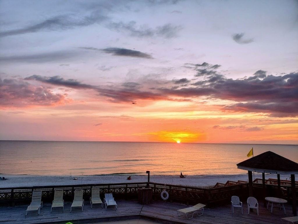 A beach scene with a sunset, a wooden pier with lounge chairs, and a small gazebo.