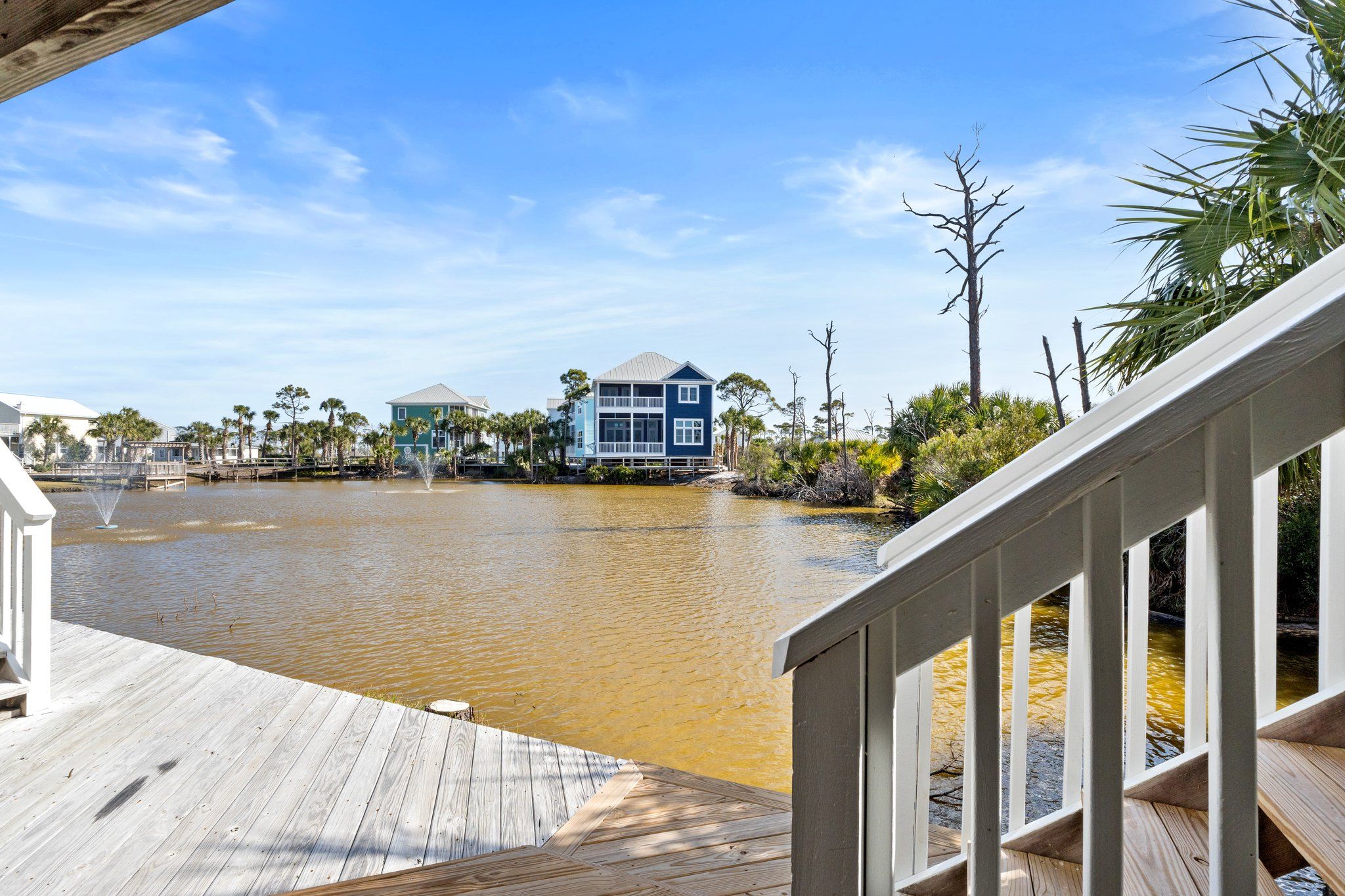 Ein Wohnhaus am Wasser mit Holzterrasse, freiem Blick auf das Wasser und mehreren Balkonen.