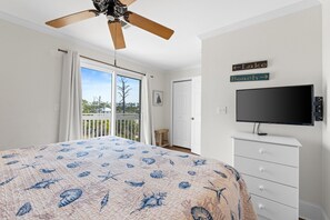 Ein Schlafzimmer mit Bett, Deckenventilator, Fernseher und einem Balkon mit Blick ins Freie.