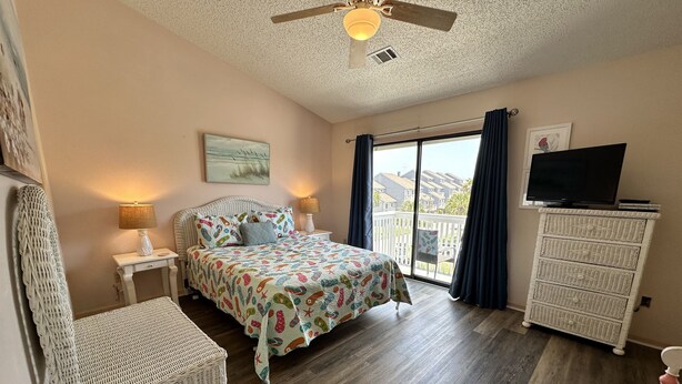 Une chambre à coucher comprenant un lit, une chaise, une commode, un téléviseur et un ventilateur de plafond.