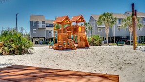 A wooden play structure on a sandy beach with a bench in the foreground and a building with balconies in the background. - Fall 2026 Rate Drop! Gulfview, 2 BR/2.5 BA, Great Location! (Port St. Joe)