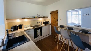 Une cuisine compacte dotée d’un plan de travail en bois, d’un four encastré, d’une machine à café et d’un coin repas avec fenêtre.