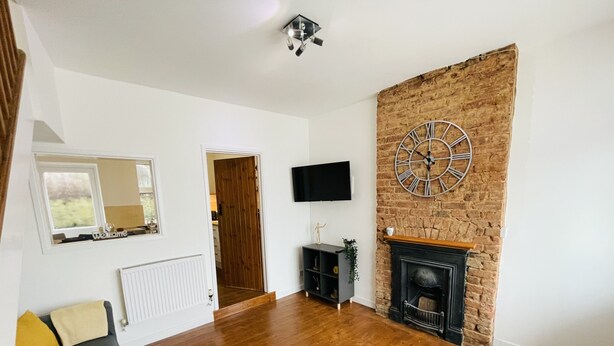Un salon spacieux doté d’un parquet, d’une cheminée, d’une horloge murale, d’un téléviseur à écran plat et d’un canapé.
