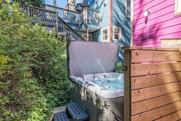 Relax in a serene outdoor setting with a hot tub surrounded by lush greenery and a wooden deck.