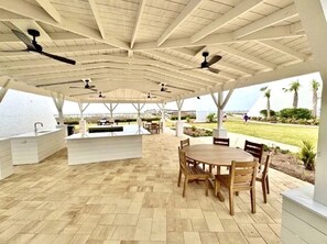An outdoor patio with a wooden table and chairs, a built-in grill, and ceiling fans.