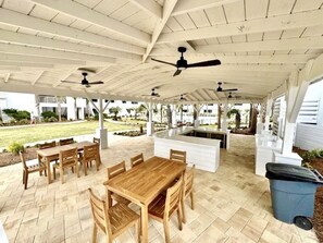 An outdoor patio with a wooden table and chairs, ceiling fans, and a trash bin.