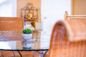 A round glass table with a small potted plant, wicker chairs, and a blurred background with a birdcage.