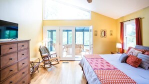 Ein Schlafzimmer mit einem Bett, einem Schminktisch, einem Schaukelstuhl, einem Deckenventilator und einem großen Fenster.