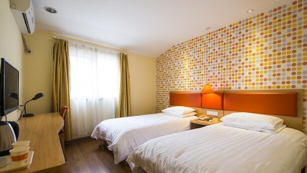 A hotel room with two beds, a desk with a computer, and a wall with a polka dot pattern.