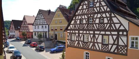 A street lined with traditional half-timbered houses, parked cars, and a clear sky.