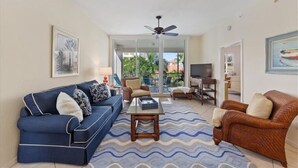 A living room with a blue sofa, a brown armchair, a wooden coffee table, and a ceiling fan. - Regatta Resort, Vanderbilt Beach, Naples, 6 minute walk to beach (Naples)