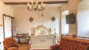 Un soggiorno tradizionale con un letto, due poltrone, un divano, un lampadario e un televisore montato a parete.