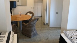 En matplats med ett runt bord och flätade stolar, ett vitt skåp med en hjärtformad dekoration och en dörr som leder till ett annat rum.