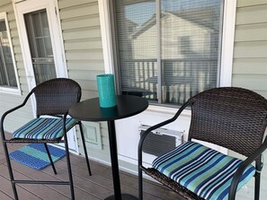 A porch with two wicker chairs, a small round table, and a teal vase.