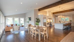 A spacious living area with a wooden dining table, a sofa, and a kitchen in the background. - Lakefront Home! Game Tables and Boat Dock (Hendersonville)
