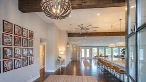 A spacious hallway with a wooden floor, a modern chandelier, and a staircase leading to a dining area with bar stools. - Lakefront Home! Game Tables and Boat Dock (Hendersonville)
