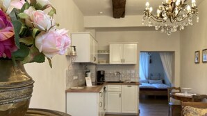 A modern kitchen with white cabinets, a dining area with a table and chairs, and a living room with a sofa and a chandelier. - Kristallzimmer - Urlaub auf dem Historischen Weingut (Maring-Noviand)