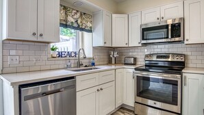 A modern kitchen with white cabinets, stainless steel appliances, a dishwasher, and a window with a 'BEACH' sign.