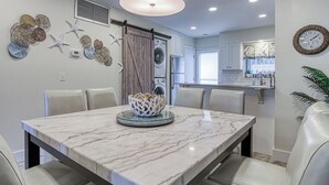 A modern kitchen with a central island, a dining area with a marble table, and a living area with a sofa.