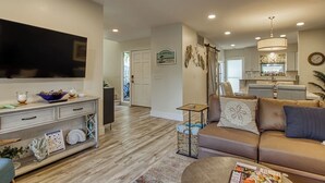 A modern living room with a flat-screen TV, a sofa, a coffee table, and a dining area in the background.