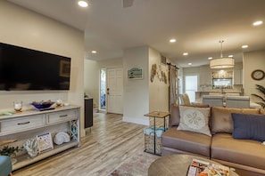 A modern living room with a flat-screen TV, a sofa, a coffee table, and a dining area in the background.