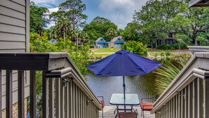 A deck with a table and chairs, overlooking a body of water and a residential area with houses.