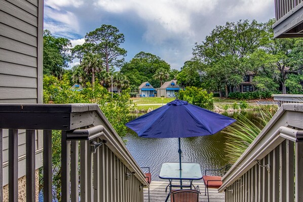A deck with a table and chairs, overlooking a body of water and a residential area with houses. - 3 min to beach, pets, outdoor shower, 1st floor master, lagoon view, near pool (Hilton Head Island)