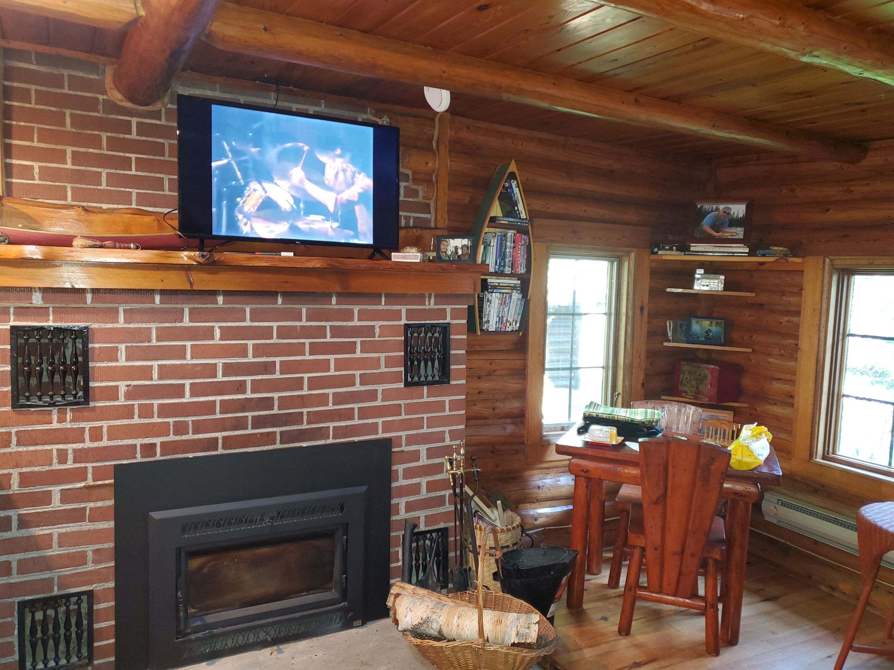 Interior acogedor de una cabaña con chimenea de ladrillo, televisor montado encima y techo de madera.