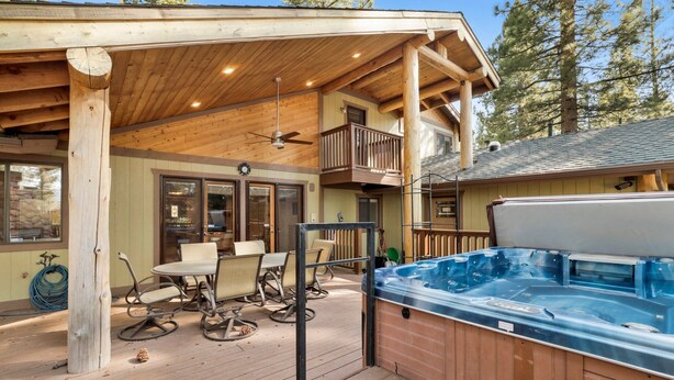 Terraza de madera con mobiliario exterior, bañera de hidromasaje y un patio cubierto con balcón.