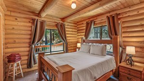 A log cabin bedroom with a bed, nightstands, and a window with curtains. - Kachina Tree House | 3BR | | Spend Spring in Flagstaff! (Flagstaff)