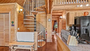 A wooden cabin interior with a spiral staircase, a kitchen area with a refrigerator, and a bench. - Kachina Tree House | 3BR | | Spend Spring in Flagstaff! (Flagstaff)