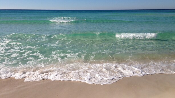 Ein Strand mit klarem türkisblauem Wasser und sanften Wellen.