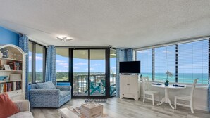 Ein geräumiges Wohnzimmer mit Balkon, einer Bücherwand, einem Fernseher und einem Essbereich mit Meerblick.