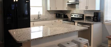 A modern kitchen with white cabinets, a black refrigerator, stainless steel appliances, and a granite countertop.