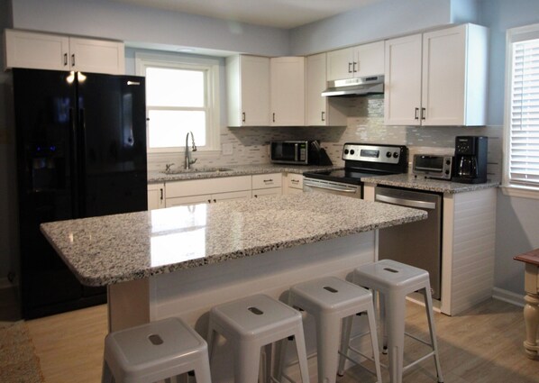 Una cocina moderna con armarios blancos, un refrigerador negro, electrodomésticos de acero inoxidable y una encimera de granito.