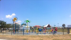 Ein Spielplatz mit verschiedenen Spielgeräten, einem umzäunten Bereich und blauem Himmel.